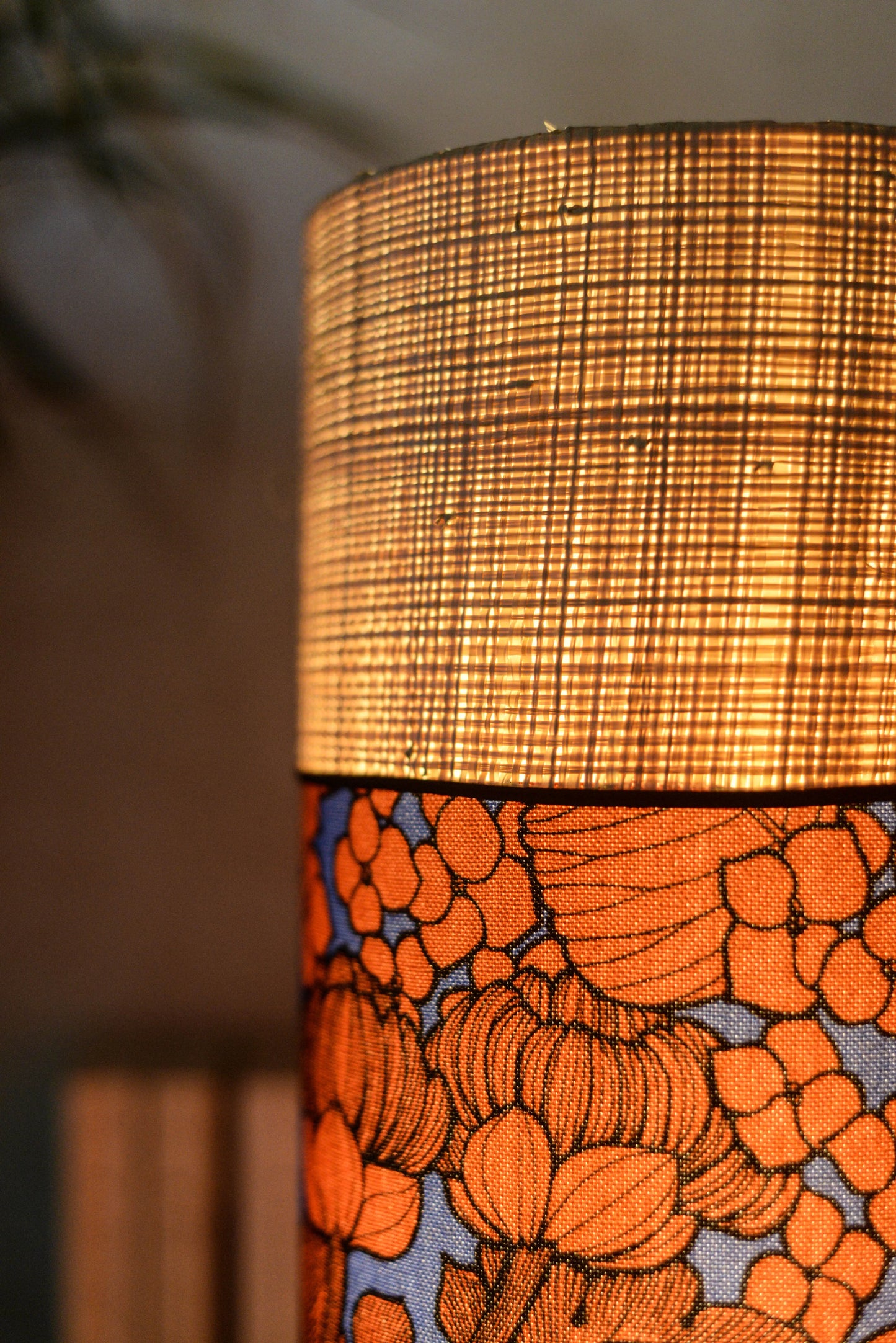 Lampe tube cynlindrique bi-matière en raphia naturel et tissu à motif de branches et fleurs orange sur fond bleu. Tissu de la collection Thevenon