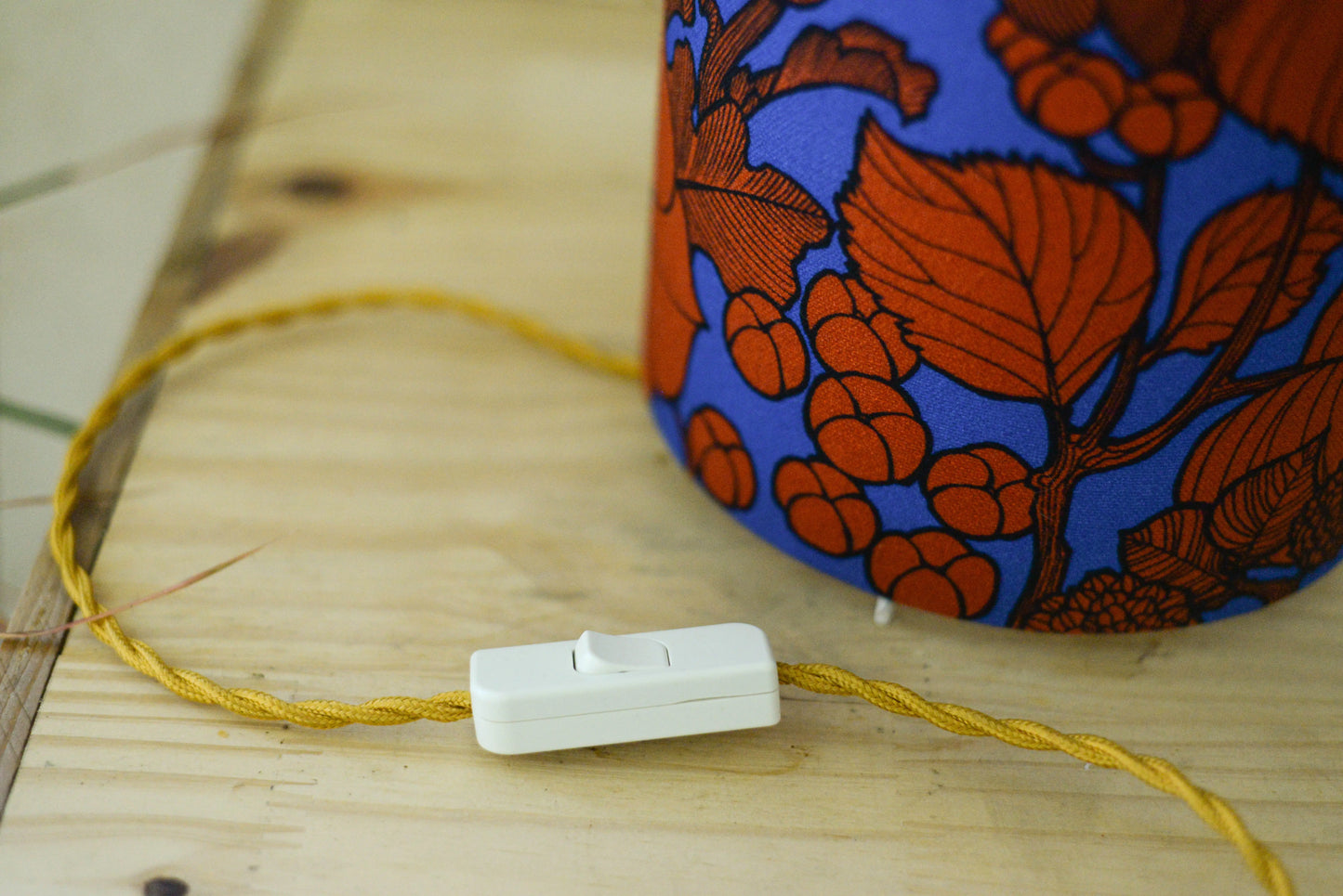 Lampe tube cynlindrique bi-matière en raphia naturel et tissu à motif de branches et fleurs orange sur fond bleu. Tissu de la collection Thevenon