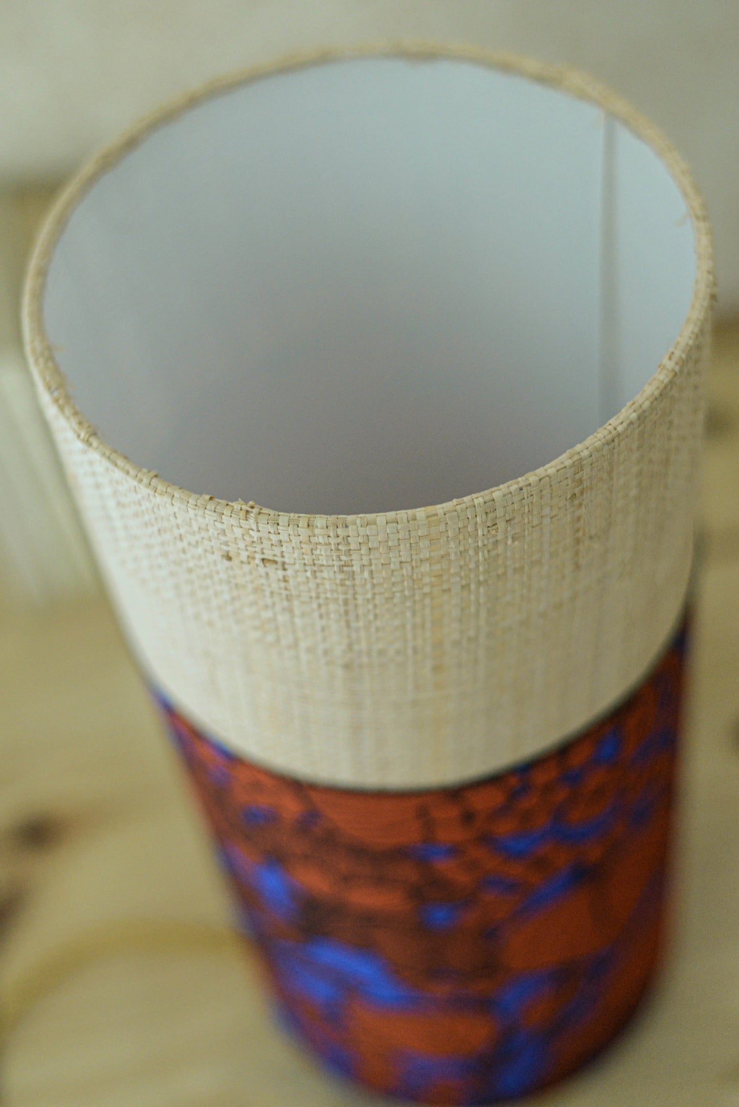 Lampe tube cynlindrique bi-matière en raphia naturel et tissu à motif de branches et fleurs orange sur fond bleu. Tissu de la collection Thevenon