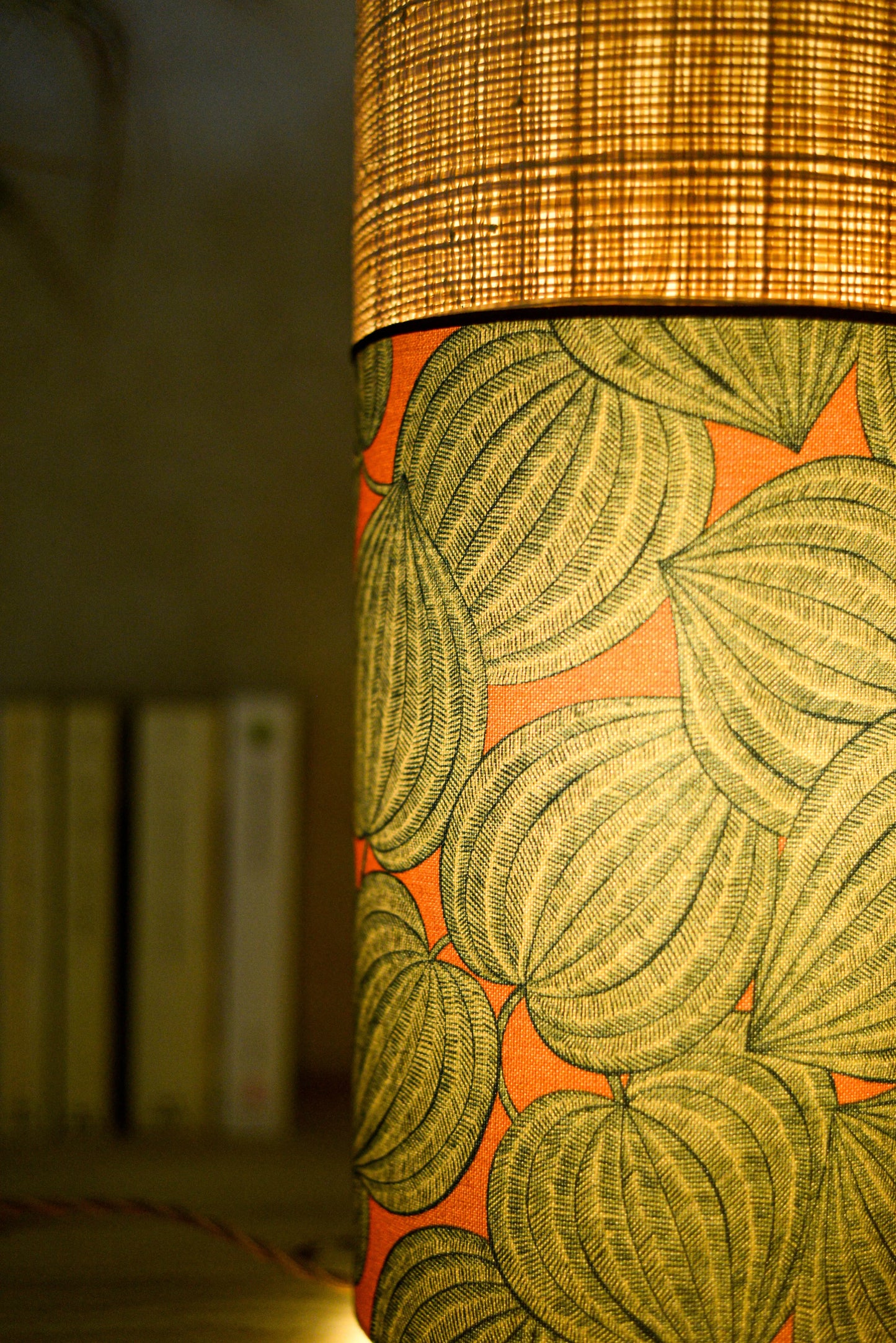 Lampe tube cynlindrique bi-matière en raphia naturel et tissu à motif de physalis bleu écru sur fond orange. Tissu de la collection Thevenon