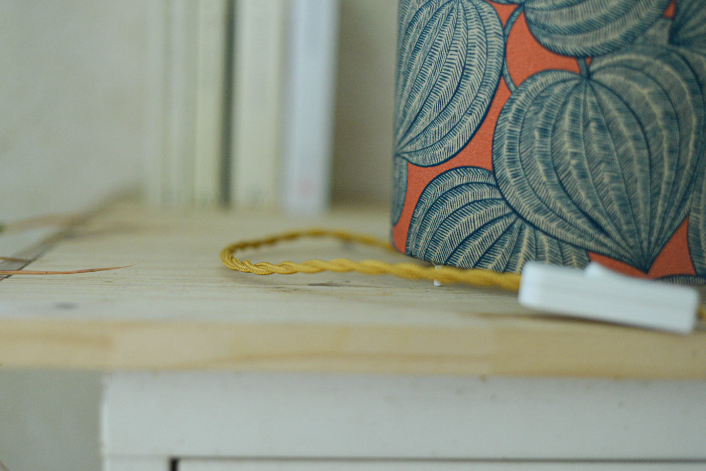 Vue du cordon torsadé doré de la lampe tube cynlindrique bi-matière en raphia naturel et tissu à motif de physalis bleu écru sur fond orange. Tissu de la collection Thevenon