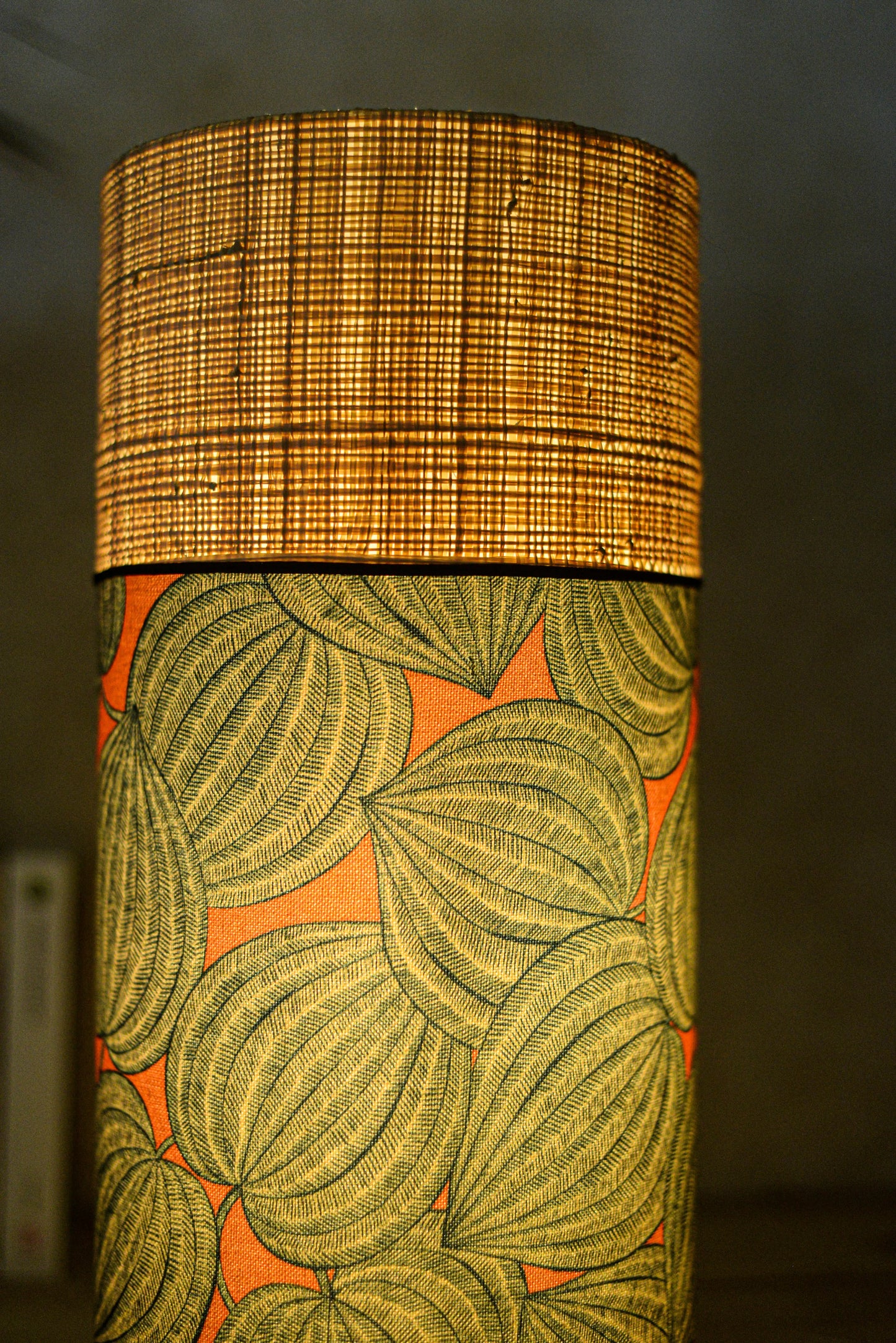 Lampe tube cynlindrique bi-matière en raphia naturel et tissu à motif de physalis bleu écru sur fond orange. Tissu de la collection Thevenon
