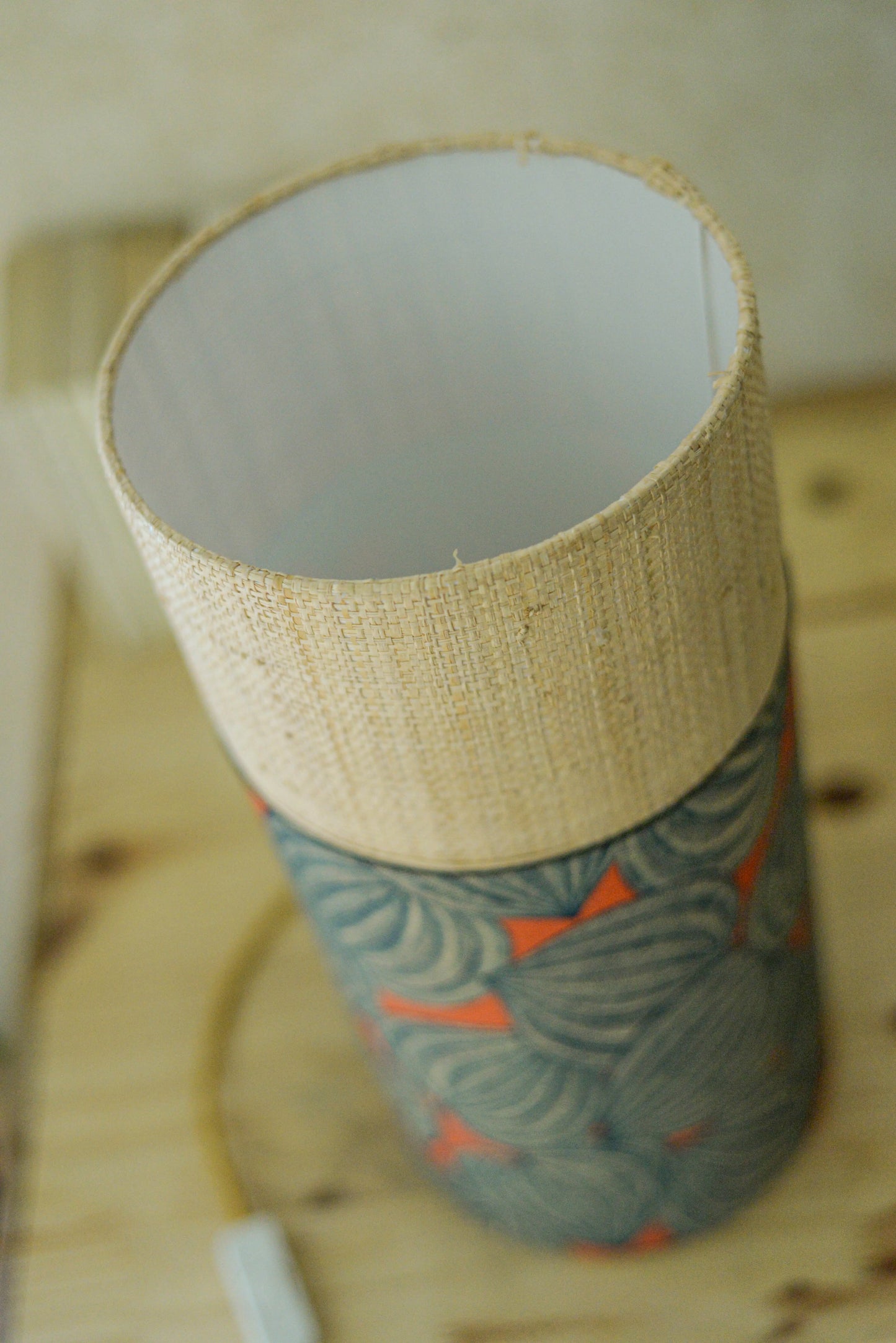 Lampe tube cynlindrique bi-matière en raphia naturel et tissu à motif de physalis bleu écru sur fond orange. Tissu de la collection Thevenon