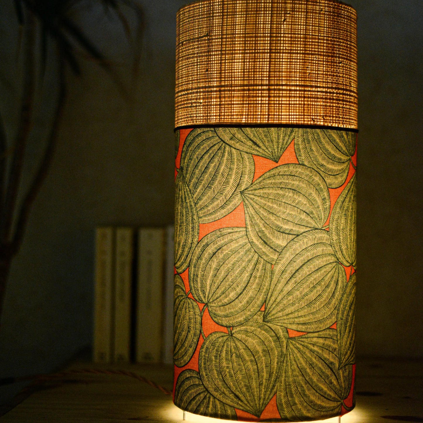 Lampe tube cynlindrique bi-matière en raphia naturel et tissu à motif de physalis bleu écru sur fond orange. Tissu de la collection Thevenon
