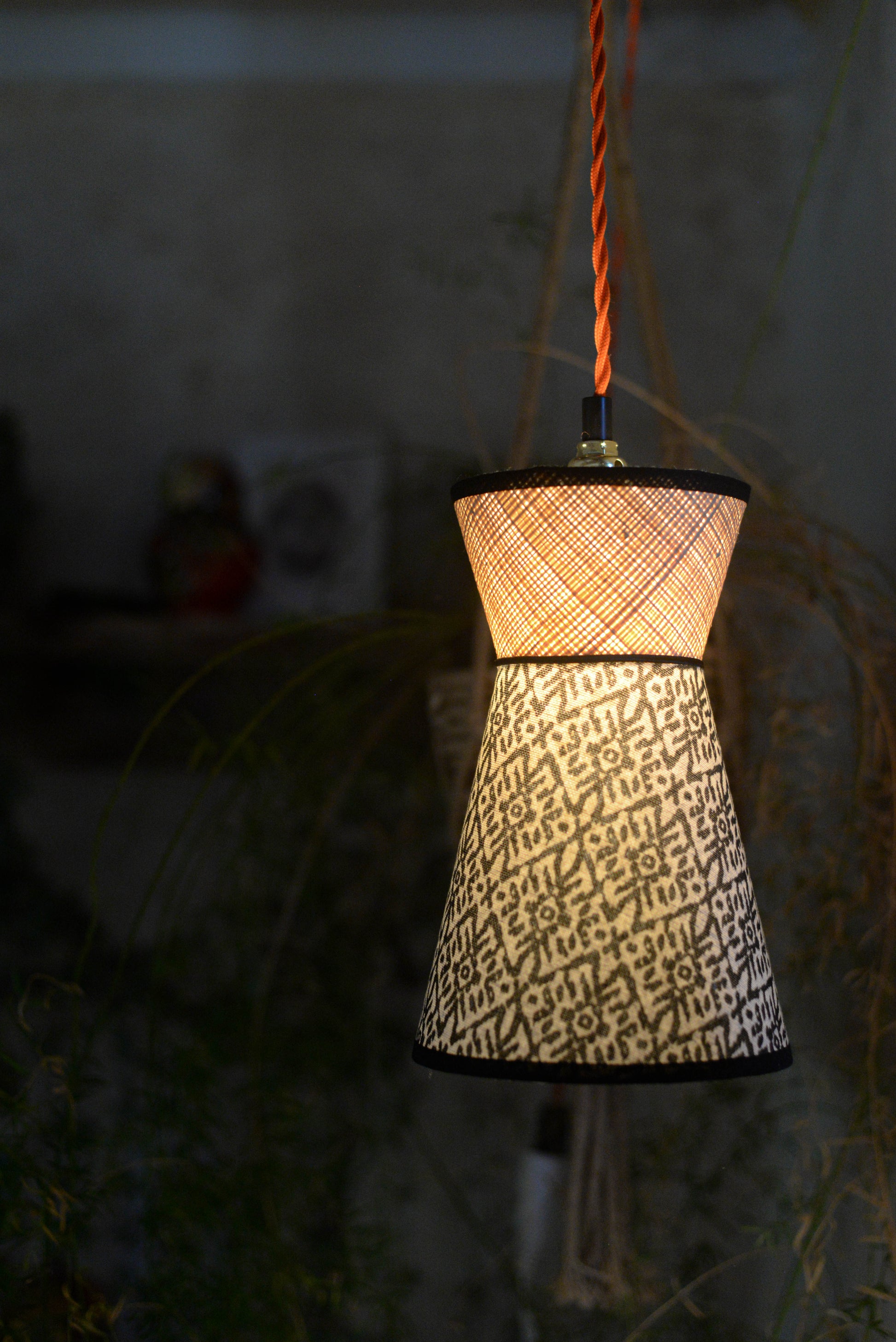 Une suspension baladeuse diabolo éclairée double cone en raphia et tissu ethnique