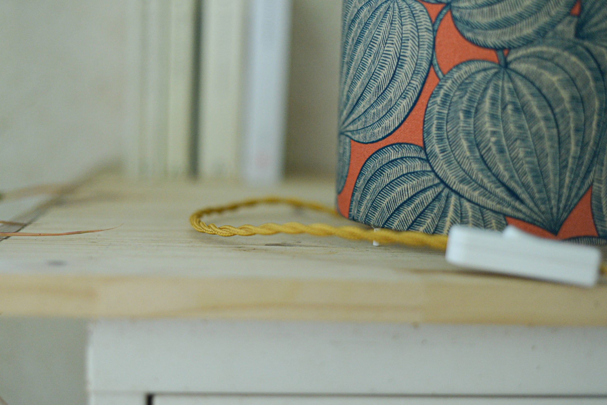 Vue du cordon torsadé doré de la lampe tube cynlindrique bi-matière en raphia naturel et tissu à motif de physalis bleu écru sur fond orange. Tissu de la collection Thevenon