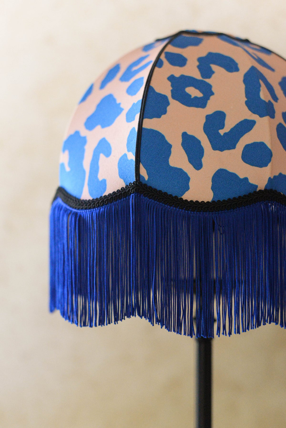 vue de profil d'un abat-jour dôme à festons en tissu léopard rose et bleu et franges bleues