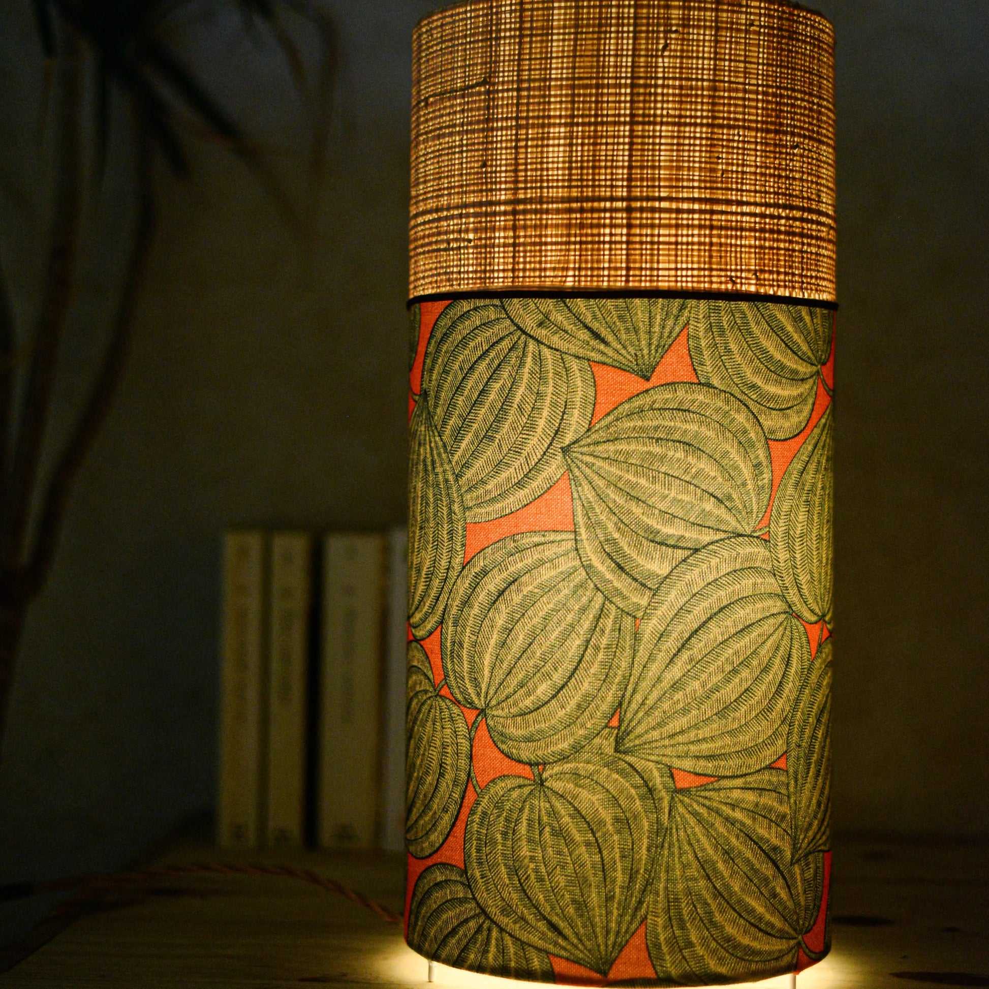 Lampe tube cynlindrique bi-matière en raphia naturel et tissu à motif de physalis bleu écru sur fond orange. Tissu de la collection Thevenon