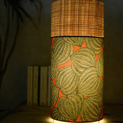 Lampe tube cynlindrique bi-matière en raphia naturel et tissu à motif de physalis bleu écru sur fond orange. Tissu de la collection Thevenon
